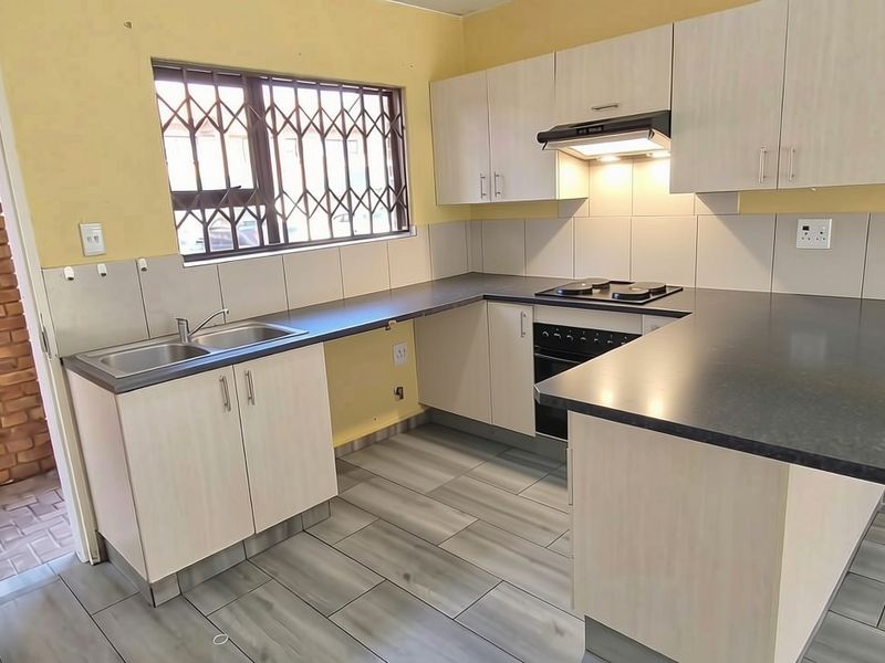 A functional kitchen featuring built-in cabinetry, a hob, oven, extractor fan, and tiled backsplash, with a breakfast bar counter and modern floor tiles.