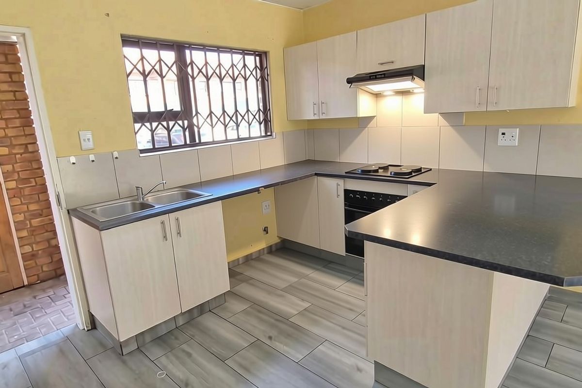 A functional kitchen featuring built-in cabinetry, a hob, oven, extractor fan, and tiled backsplash, with a breakfast bar counter and modern floor tiles.
