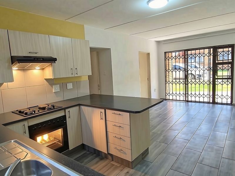Open-plan kitchen and living area featuring modern cabinetry, built-in oven, gas hob, and tiled flooring, leading to a secure exterior entrance.