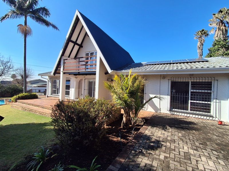Rear view of an A-frame house featuring a tiled patio, balcony, solar panels, and paved outdoor area.