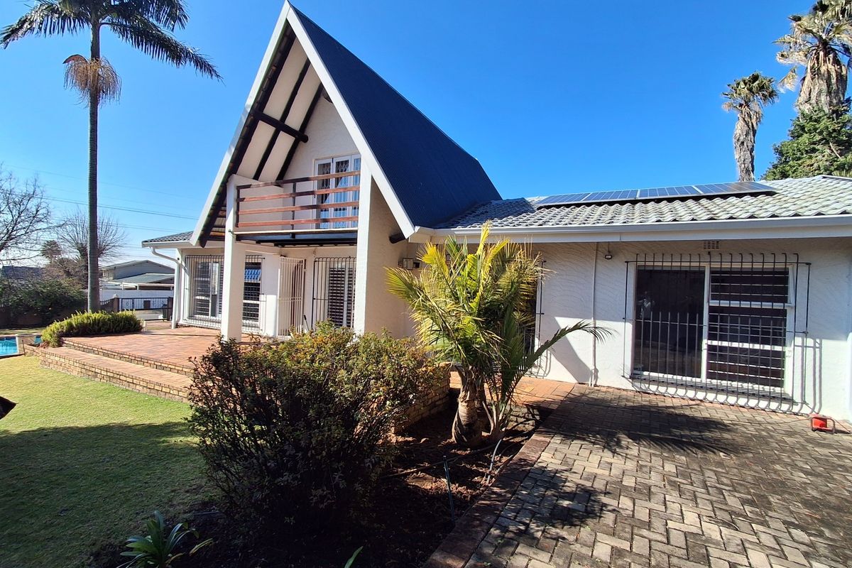 Rear view of an A-frame house featuring a tiled patio, balcony, solar panels, and paved outdoor area.