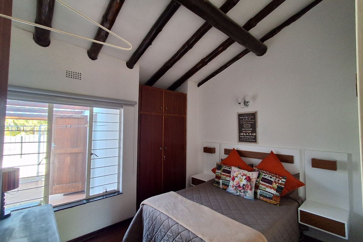 A cozy bedroom featuring exposed timber ceiling beams, built-in wooden cabinetry, laminate flooring, and direct access to an outdoor patio area.