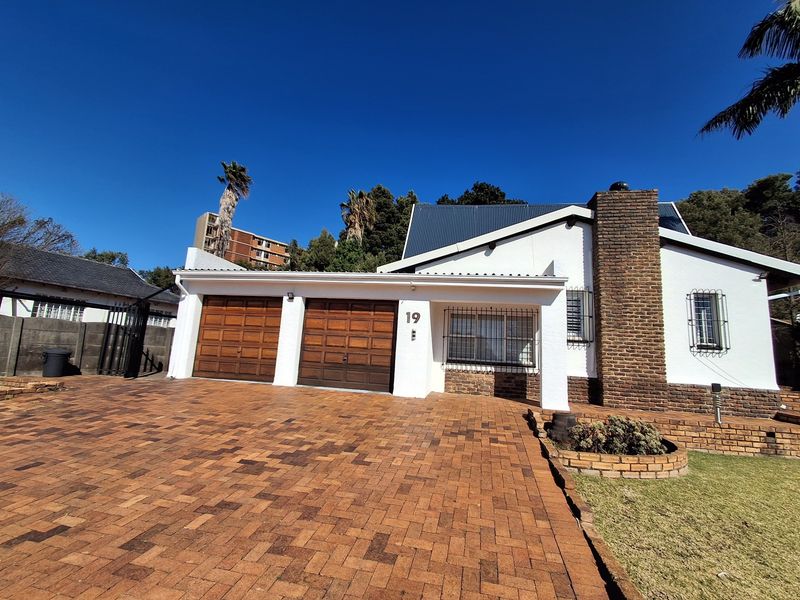 Front elevation of a house featuring a double garage, brick chimney, and a paved driveway with established garden elements.