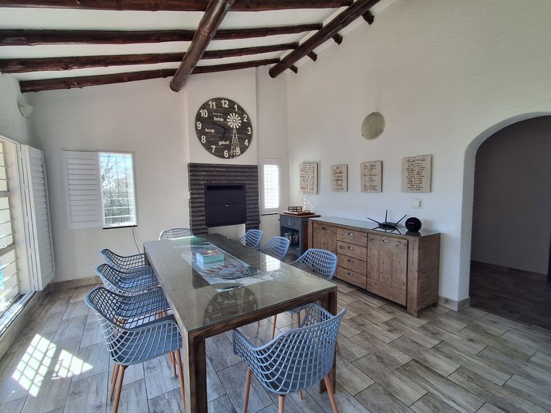 Spacious dining room featuring exposed timber ceiling beams, tiled flooring, a built-in fireplace, and plantation shutters, creating a warm and inviting atmosphere.