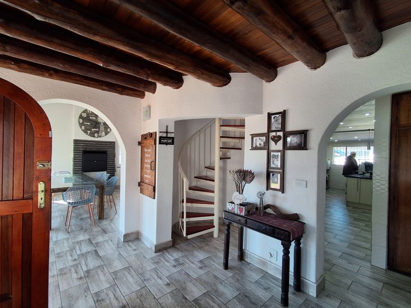 Welcoming entry hall featuring rustic exposed timber ceiling beams, arched architectural transitions, and a central spiral staircase leading to the upper level.