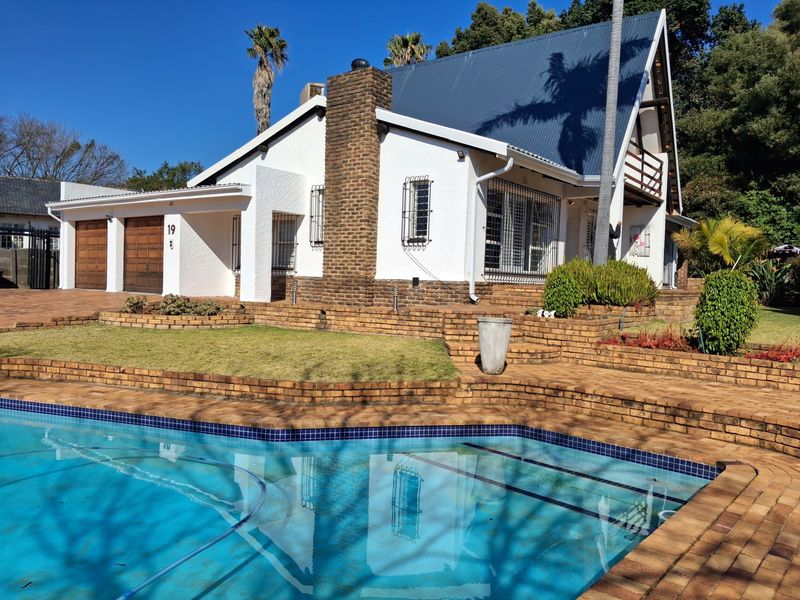 Rear view of the property featuring a swimming pool, paved patio area, brick chimney, and double garage with a metal roof.
