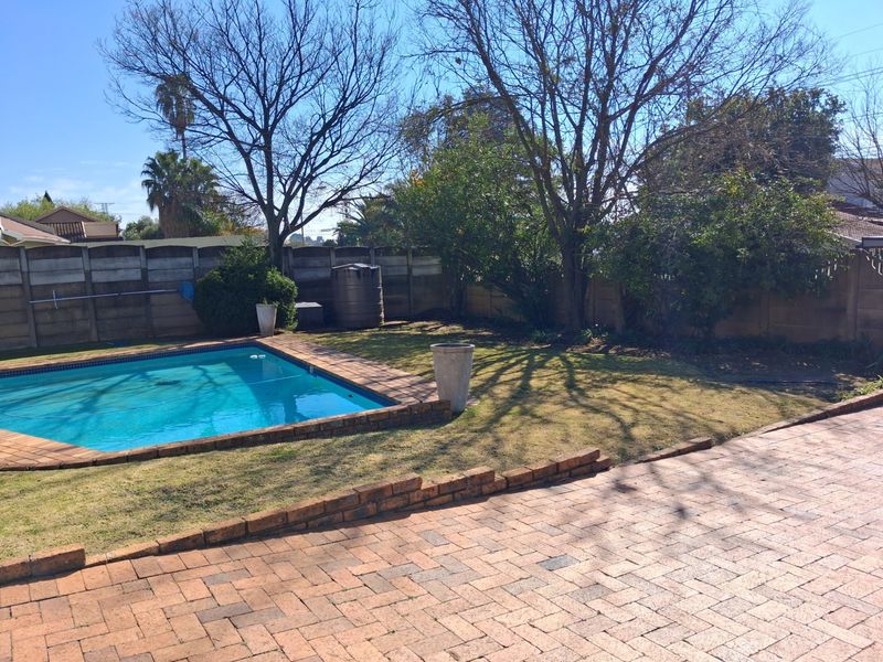 Outdoor pool area featuring a swimming pool, brick paved patio, and a lawn enclosed by a precast concrete boundary wall.