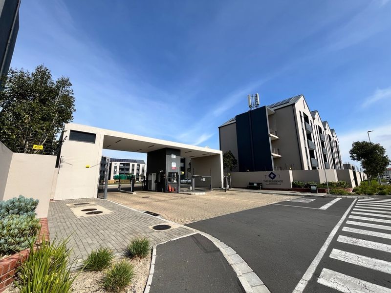 The secure entrance to The Residence apartment complex, featuring a modern gatehouse, boom gate access, and well-maintained paved driveway and exterior facade.