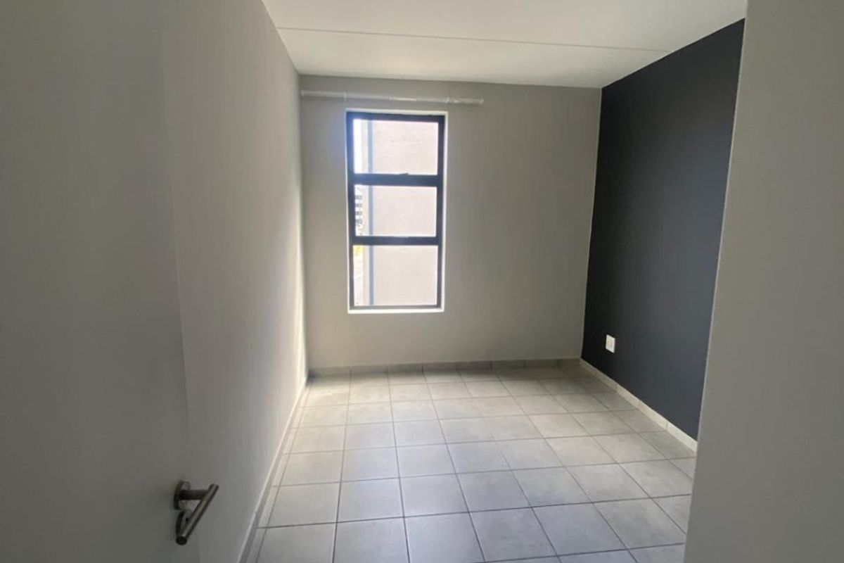 A clean, empty bedroom featuring neutral tiled flooring, a modern dark accent wall, and a large window providing natural light.
