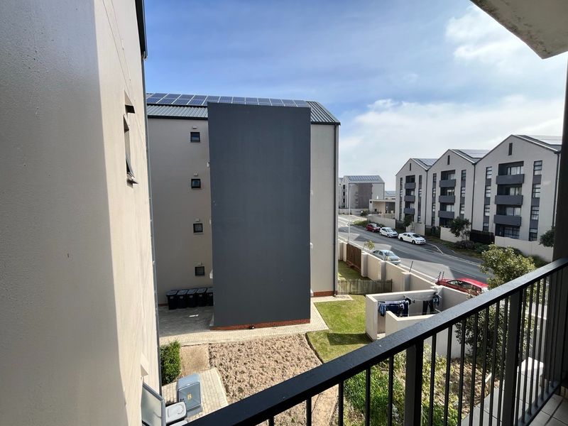 An elevated view from a balcony overlooking the apartment complex grounds, street, and neighboring residential buildings.