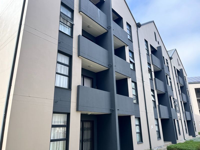 A modern multi-story apartment building facade featuring a contemporary grey and beige color scheme with private balconies and secure window access.