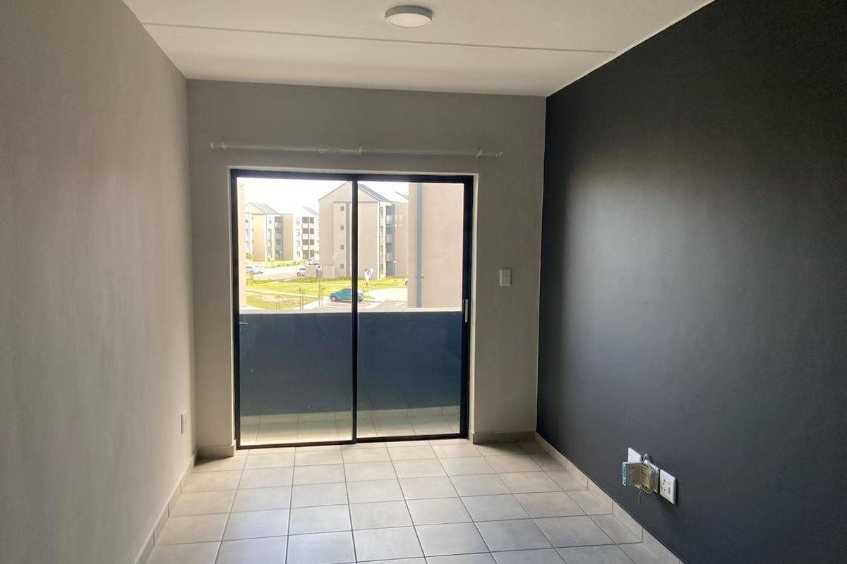An empty living room featuring neutral tiled flooring, a dark accent wall, and a sliding glass door leading to a balcony.