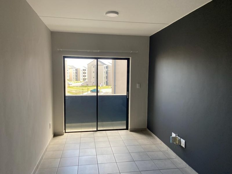 An empty living room featuring neutral tiled flooring, a dark accent wall, and a sliding glass door leading to a balcony.