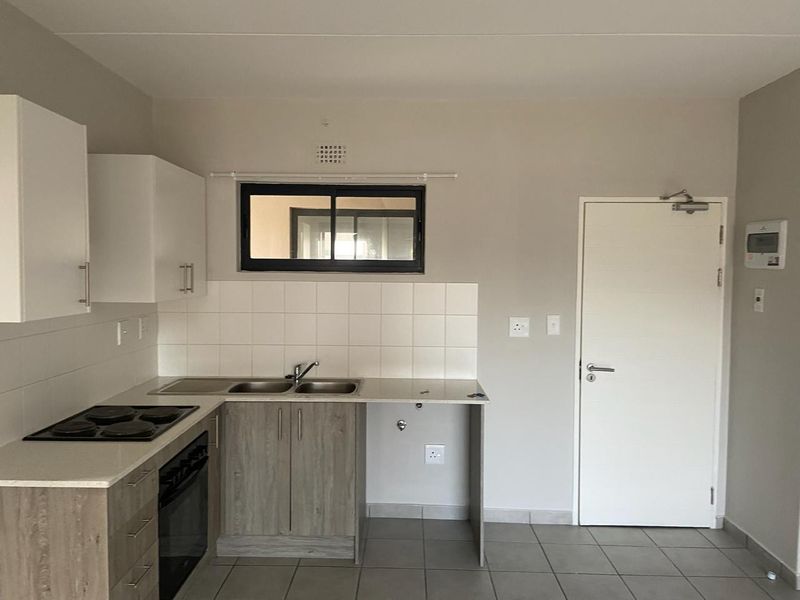 A clean, modern kitchen featuring built-in cabinetry, a stainless steel sink, electric hob, oven, and tiled flooring, offering a functional and well-maintained workspace.