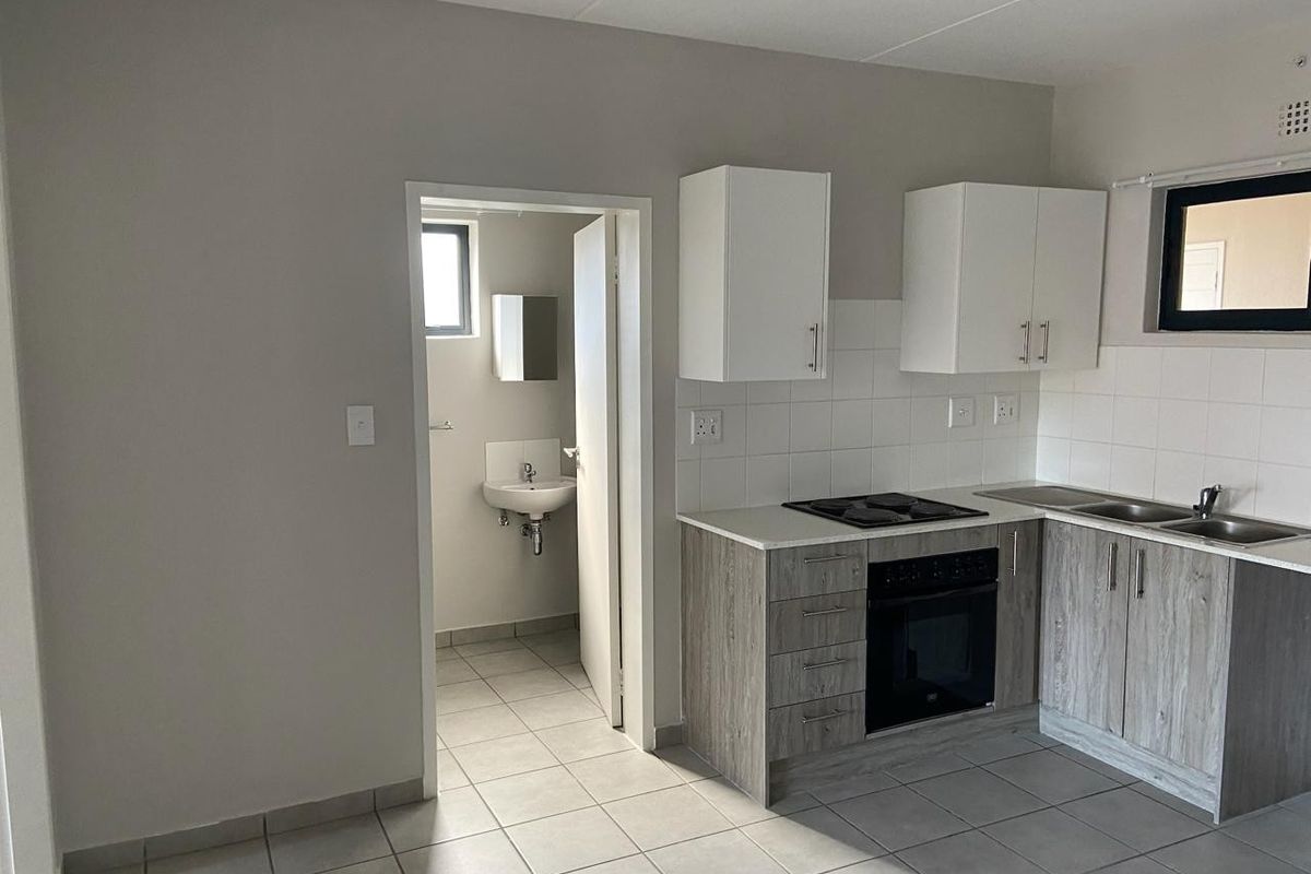 A clean, functional kitchen featuring modern wood-look cabinetry, built-in oven and hob, tiled backsplash, and adjacent access to a small bathroom.