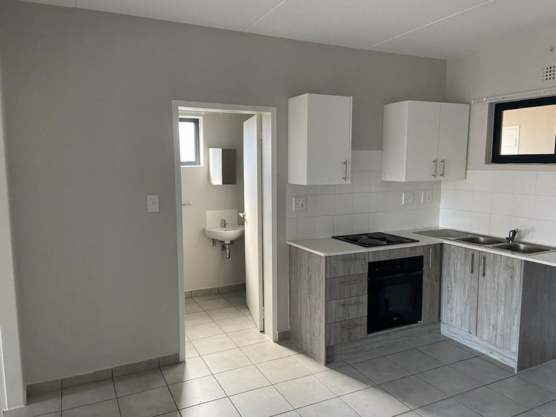 A clean, functional kitchen featuring modern wood-look cabinetry, built-in oven and hob, tiled backsplash, and adjacent access to a small bathroom.