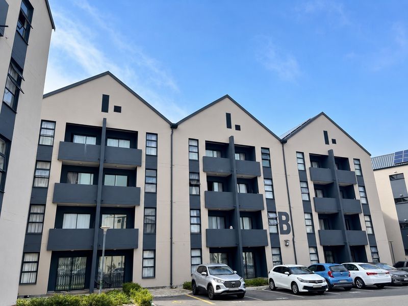 Front elevation of a modern multi-story apartment complex featuring private balconies, neutral facade finishes, and dedicated ground-level parking.