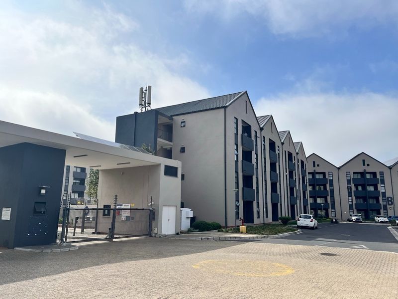 Modern apartment complex exterior featuring a secure gated entrance, paved driveway, and multi-story residential blocks with private balconies.