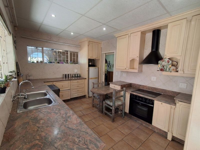Functional kitchen featuring built-in cabinetry, electric oven, hob with extractor fan, double basin sink, and tiled flooring with a neutral backsplash.