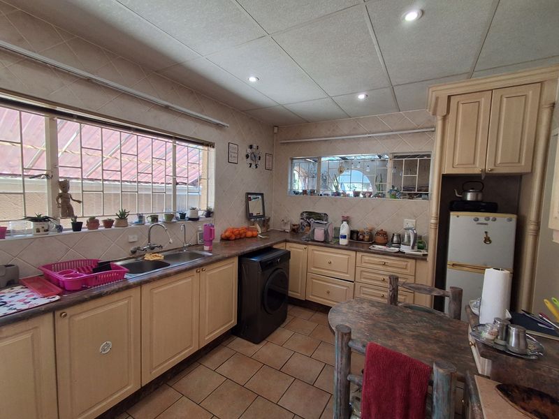 A functional kitchen featuring laminate cabinetry, tiled backsplash, double basin sink, and tiled flooring, offering a practical layout with ample natural light.