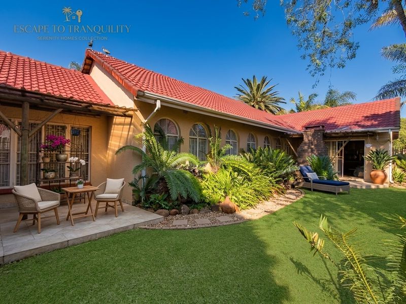 A well-maintained rear exterior view featuring a tiled roof, arched windows, a brick chimney, and a paved patio area overlooking a landscaped garden.