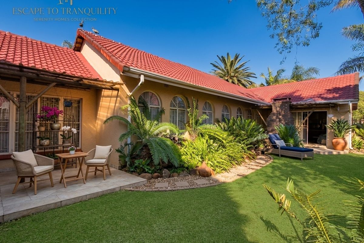 A well-maintained rear exterior view featuring a tiled roof, arched windows, a brick chimney, and a paved patio area overlooking a landscaped garden.
