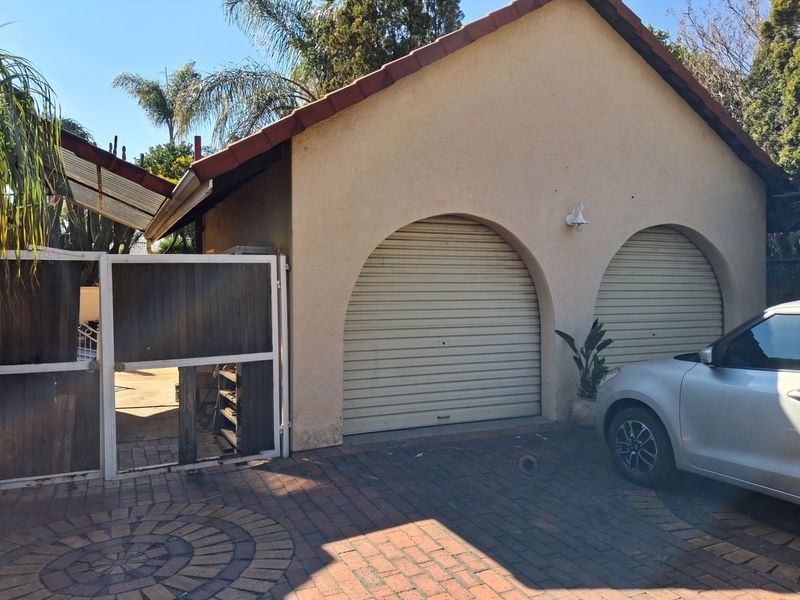 Exterior view of a double garage featuring arched openings, roller doors, and a paved driveway with an adjacent pedestrian gate.