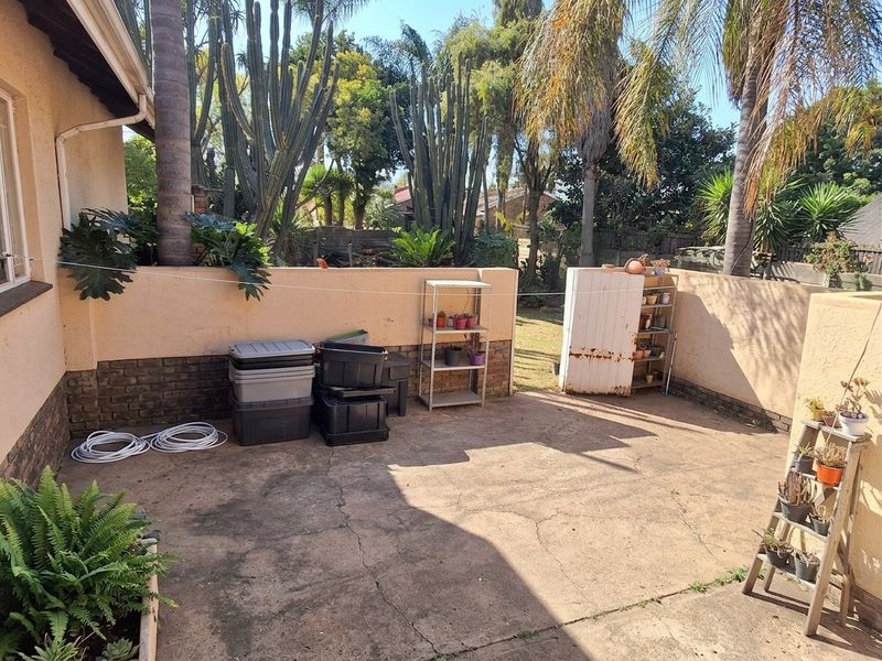 A paved outdoor patio area featuring masonry boundary walls and established garden surroundings, offering a functional space for outdoor living.
