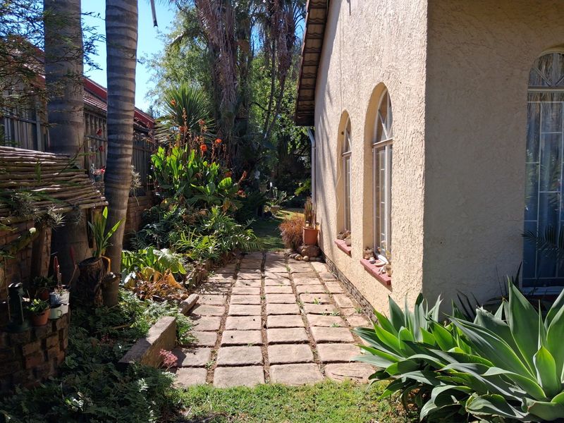 A side garden path featuring paved stones alongside the exterior wall of the house with arched windows and mature landscaping.