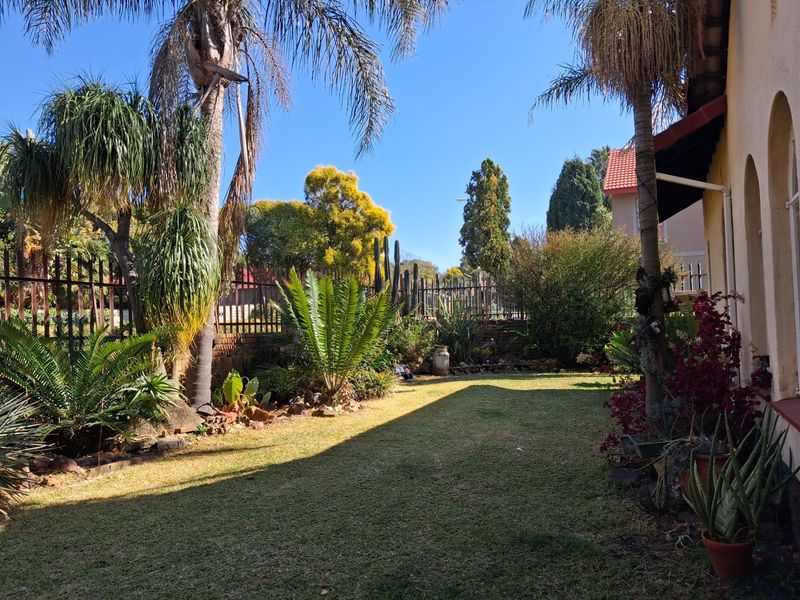 A well-maintained private garden featuring mature palm trees, established landscaping, and secure perimeter fencing.