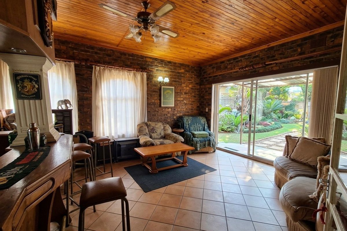 Spacious living room featuring exposed brick walls, a timber ceiling, and a built-in bar, with large sliding doors opening to a landscaped garden.