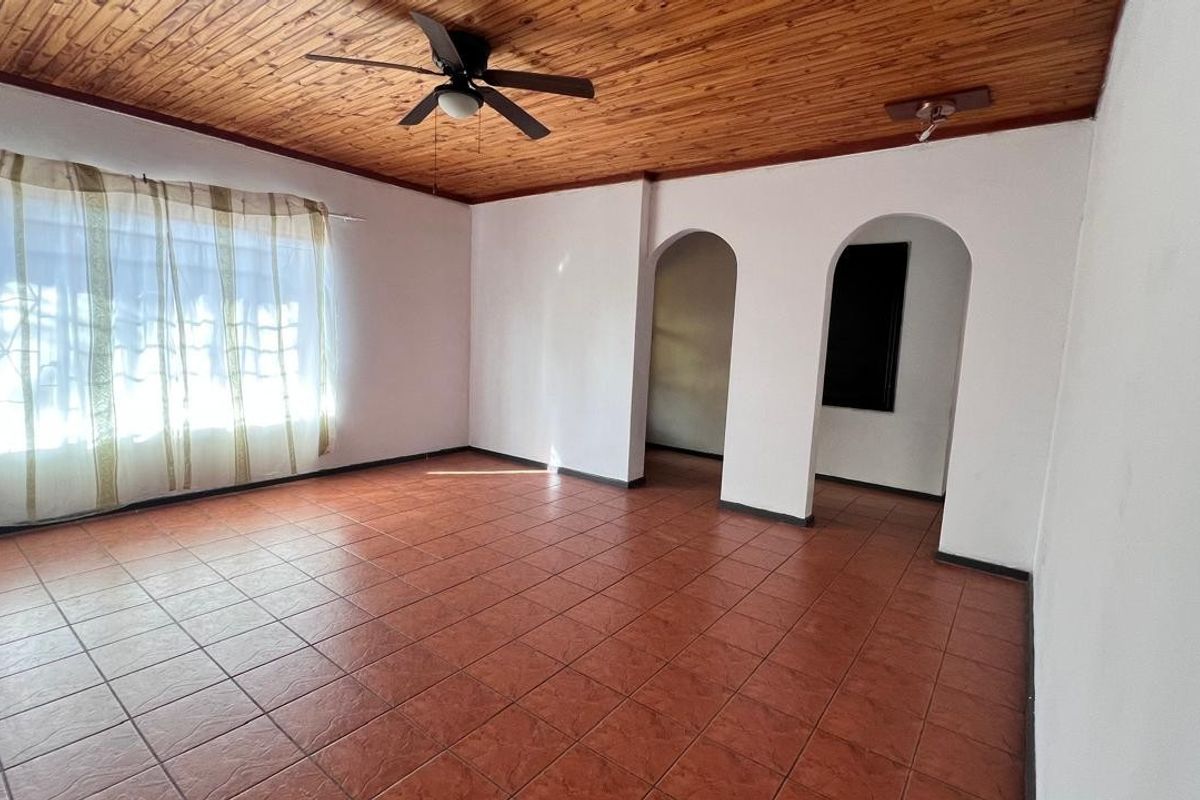 Spacious living area featuring a warm timber-clad ceiling, ceiling fan, and durable ceramic floor tiles, with distinctive arched doorways leading to adjacent rooms.