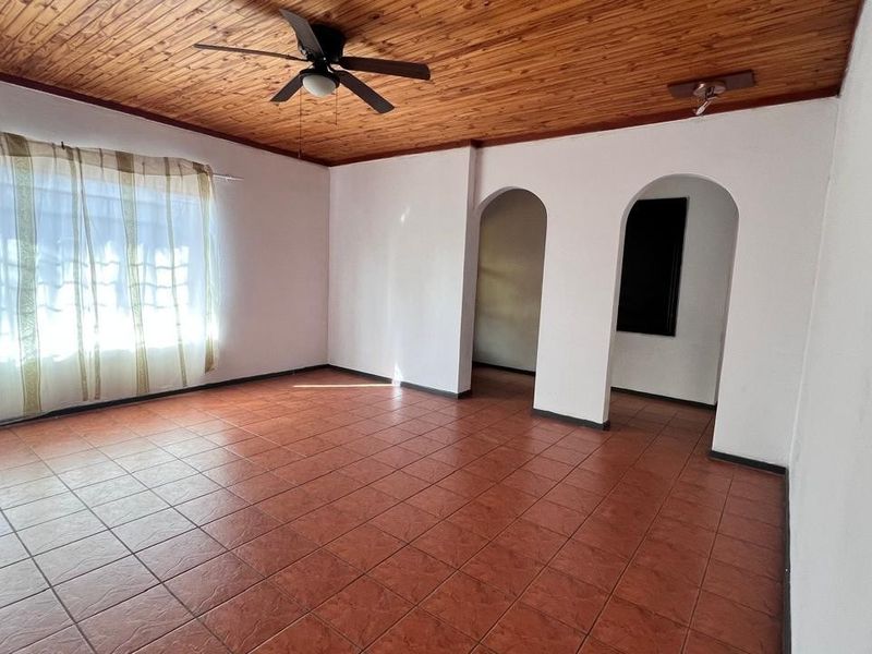 Spacious living area featuring a warm timber-clad ceiling, ceiling fan, and durable ceramic floor tiles, with distinctive arched doorways leading to adjacent rooms.