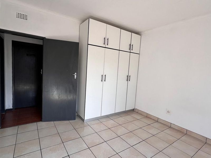 A simple, empty bedroom featuring tiled flooring and a built-in white wardrobe, providing a clean and functional space ready for personalization.