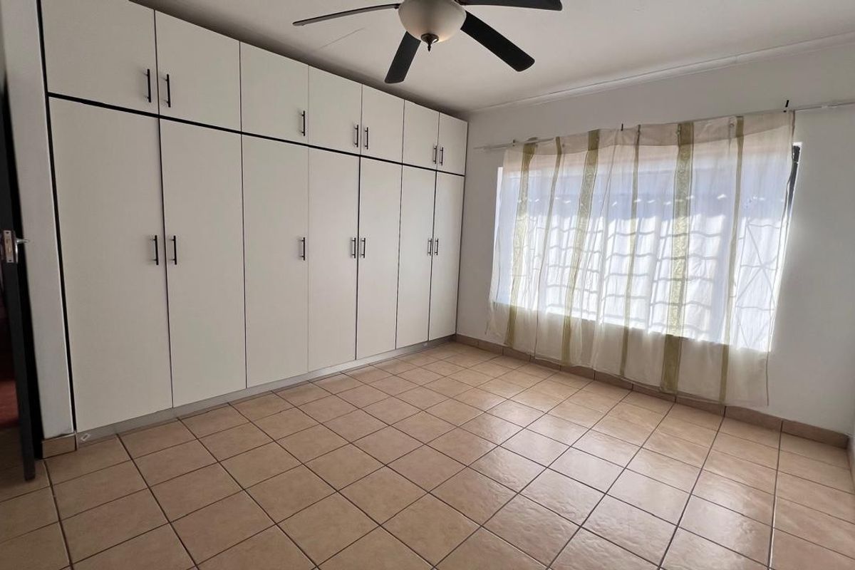 A spacious bedroom featuring extensive floor-to-ceiling built-in cupboards, tiled flooring, and a ceiling fan.