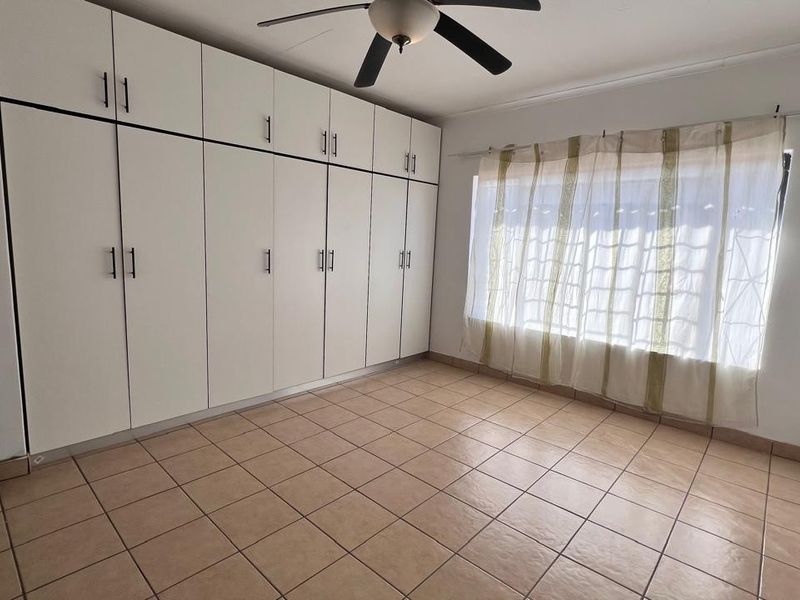 A spacious bedroom featuring extensive floor-to-ceiling built-in cupboards, tiled flooring, and a ceiling fan.
