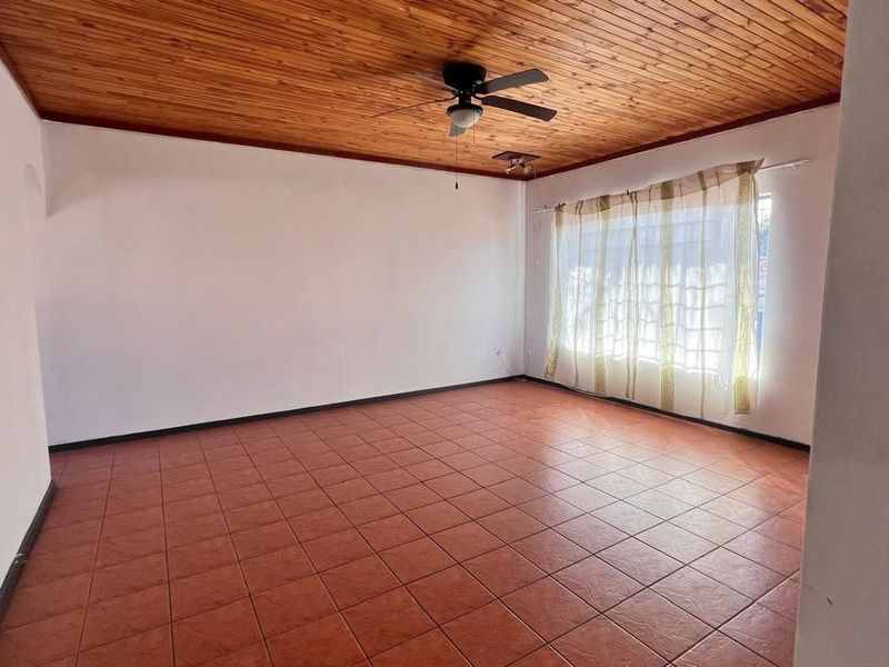 Spacious living area featuring a warm timber tongue and groove ceiling, ceiling fan, and durable ceramic floor tiles throughout.