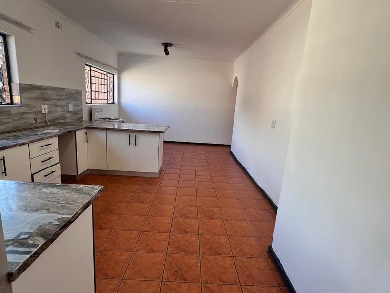A functional, empty kitchen featuring white cabinetry, laminate countertops, and tiled flooring, offering a blank canvas for potential updates.