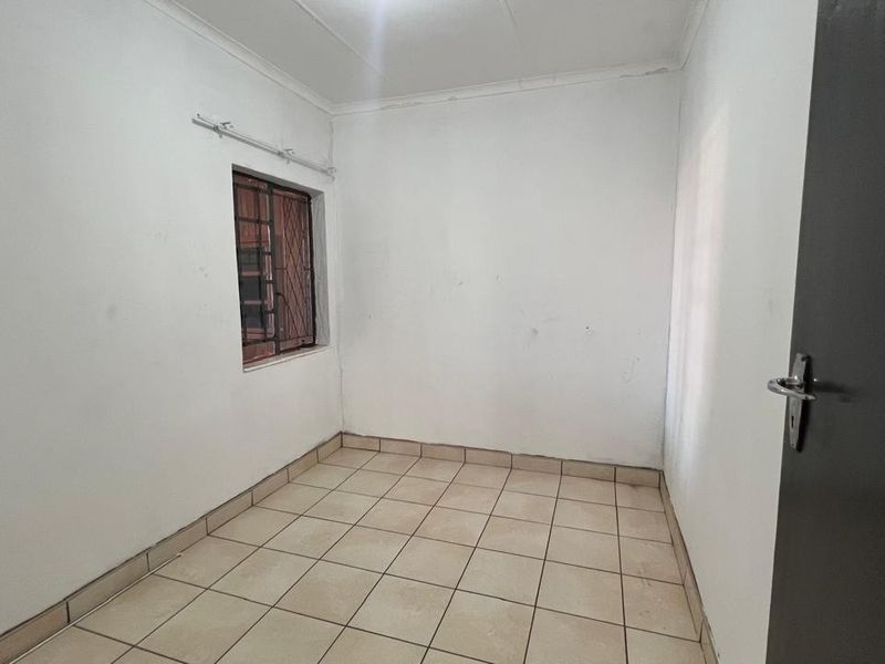 An empty bedroom featuring tiled flooring and a window with security bars, presenting a blank canvas for potential interior design updates.