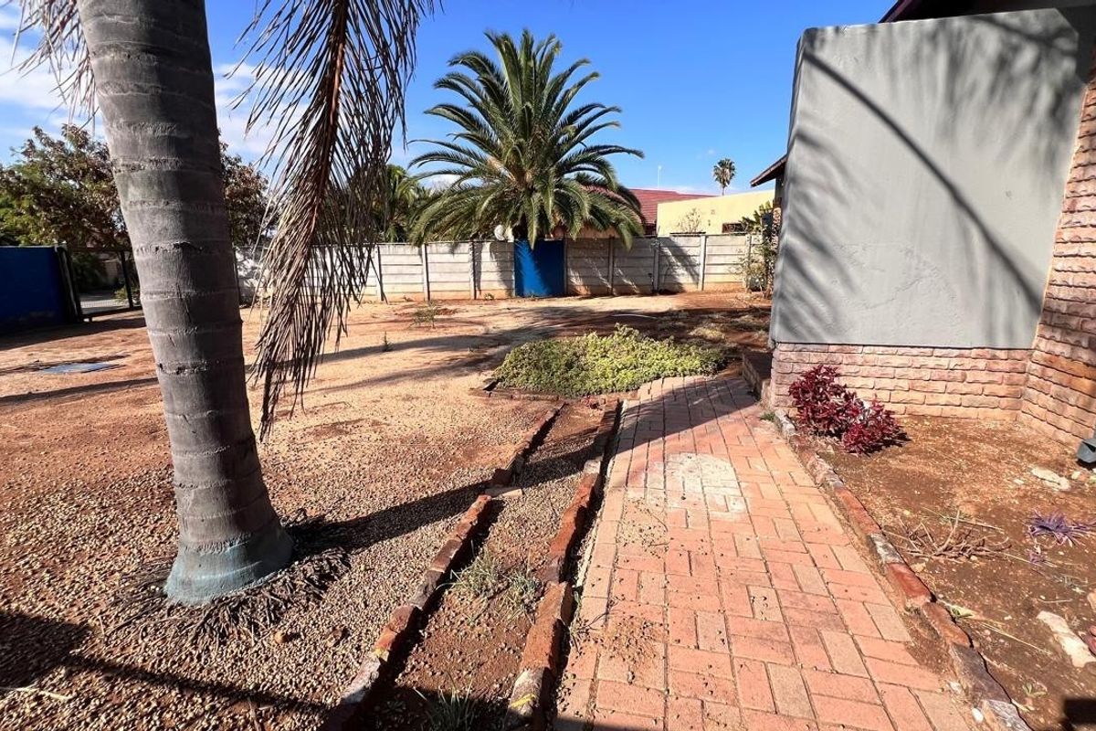 A spacious rear garden area featuring brick paving, a precast boundary wall, and established palm trees, offering potential for landscaping and outdoor improvement.