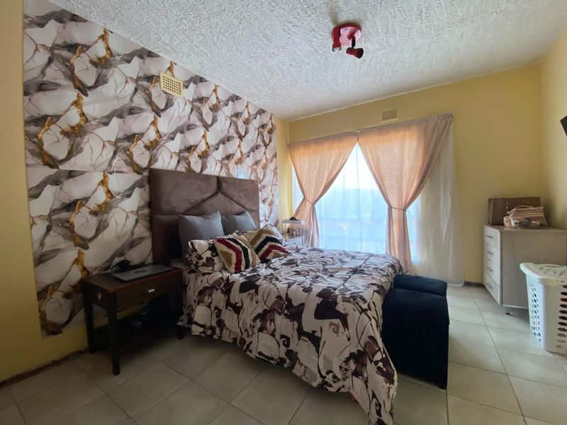 A bedroom featuring tiled flooring, a textured ceiling, and a decorative feature wall, offering a functional space with potential for modern updates.