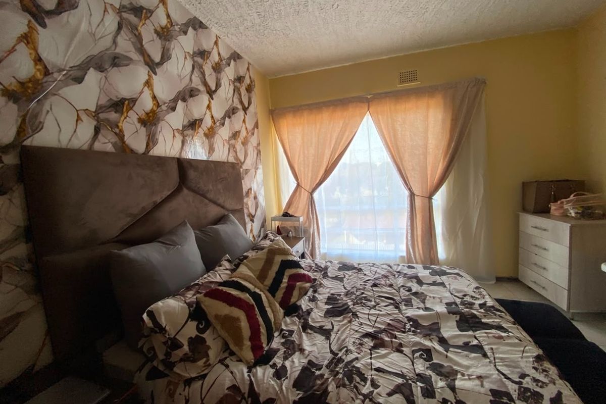 A bedroom featuring a textured ceiling, ventilation grille, and large window with curtains, providing natural light to the space.