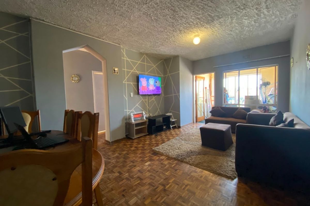 A living room featuring traditional parquet flooring, a textured ceiling, and an archway leading to an adjacent space, with natural light from a large window.
