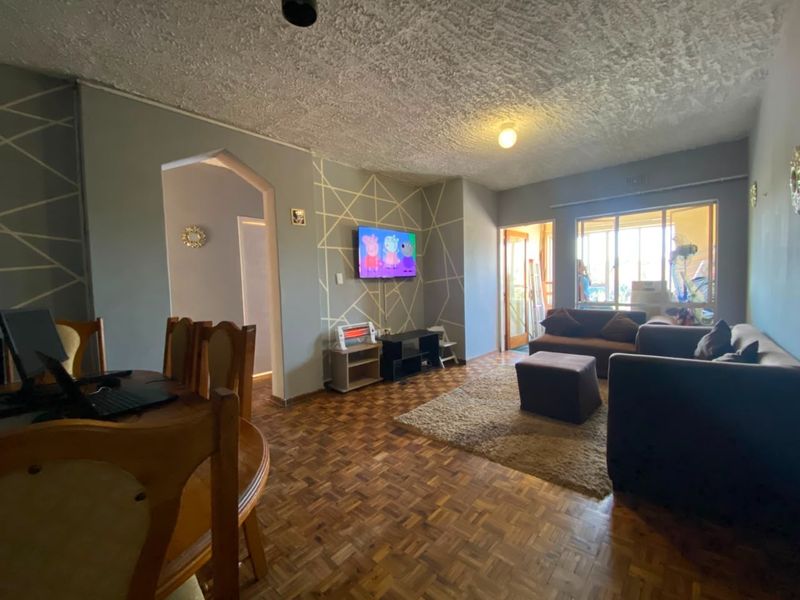 A living room featuring traditional parquet flooring, a textured ceiling, and an archway leading to an adjacent space, with natural light from a large window.