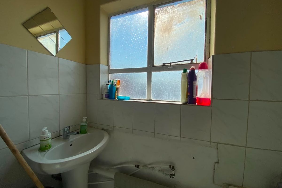 A dated bathroom featuring a pedestal basin with exposed plumbing and tiled splashback, requiring renovation to improve functionality and aesthetic appeal.