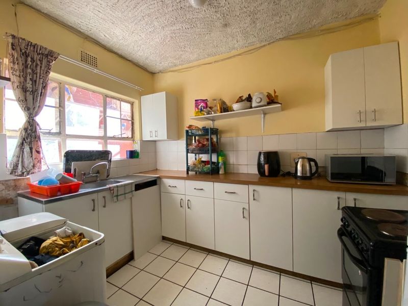 A functional kitchen featuring white cabinetry, laminate countertops, tiled backsplash, and ceramic flooring, offering a practical layout with potential for modern updates.