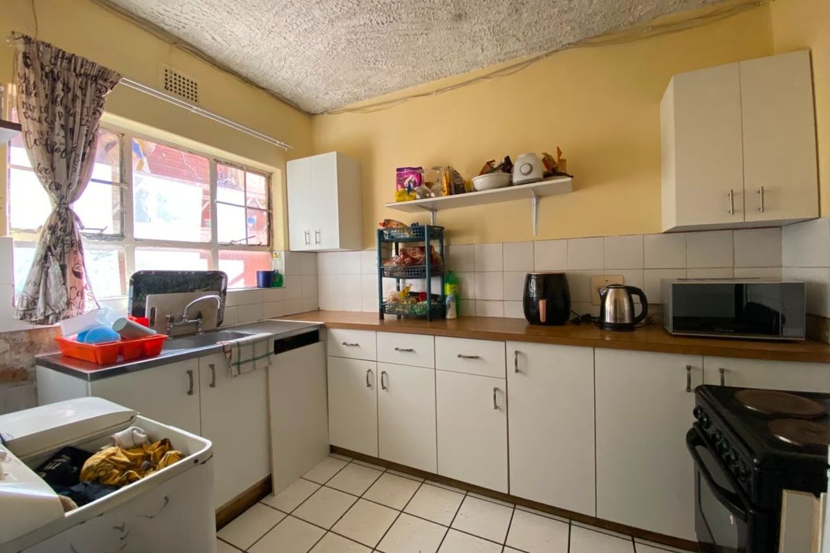 A functional kitchen featuring white cabinetry, laminate countertops, tiled backsplash, and ceramic flooring, offering a practical layout with potential for modern updates.