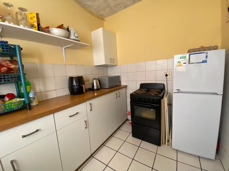 Compact kitchen featuring white cabinetry, tiled backsplash, laminate countertops, and a freestanding stove, requiring some cosmetic updates to the ceiling and finishes.