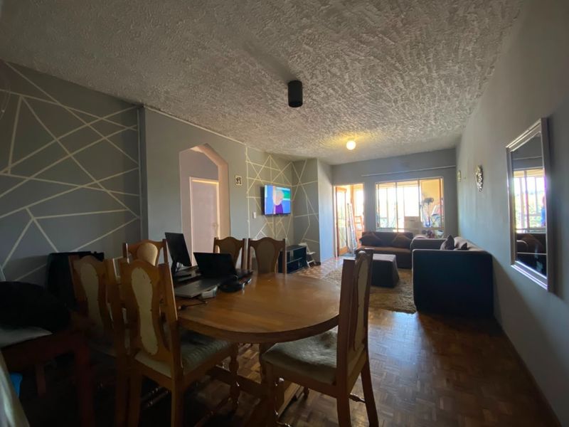 Open plan living and dining area featuring parquet flooring, a textured ceiling, and an archway leading to other parts of the apartment.