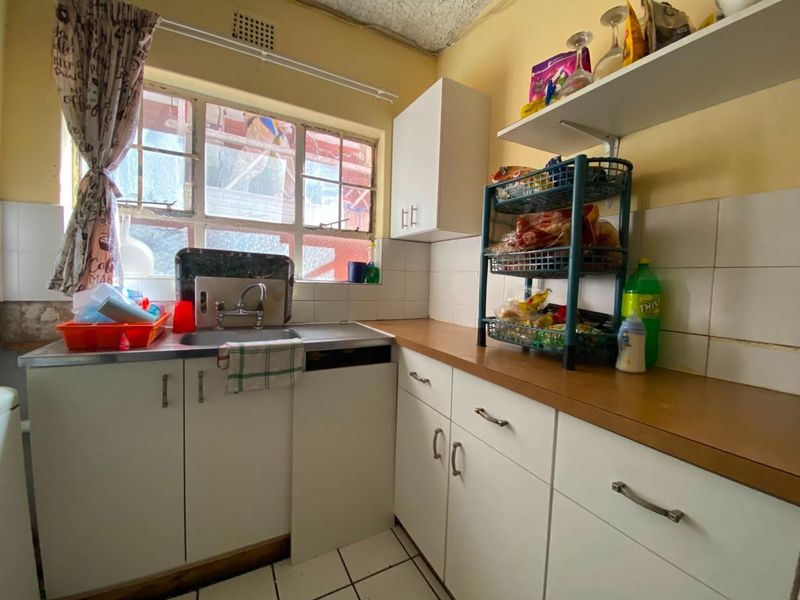 A compact kitchen featuring white cabinetry, laminate countertops, tiled backsplash, and a stainless steel sink, requiring cosmetic updates to modernize the space.